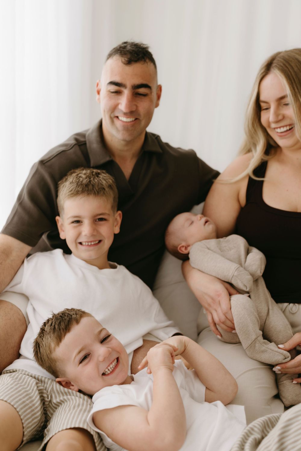 Smiling family of five with two boys and newborn baby sitting together.