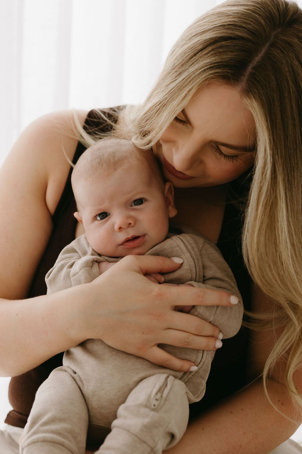 Blonde mother tenderly holding and gazing at alert newborn baby in arms.