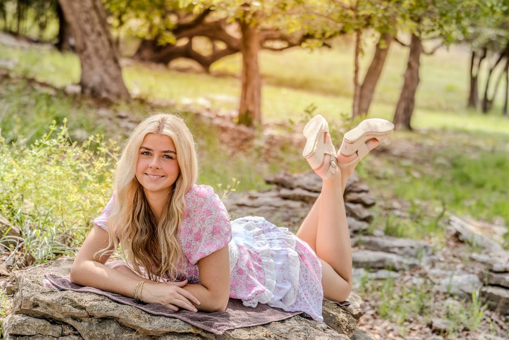 Person in pink floral dress laying on rocks outdoors during a sunny summer day in nature.