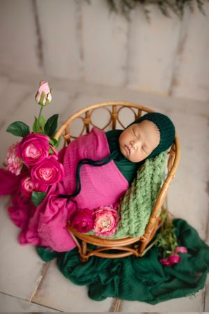 Newborn photography setup with rattan chair and pink roses.