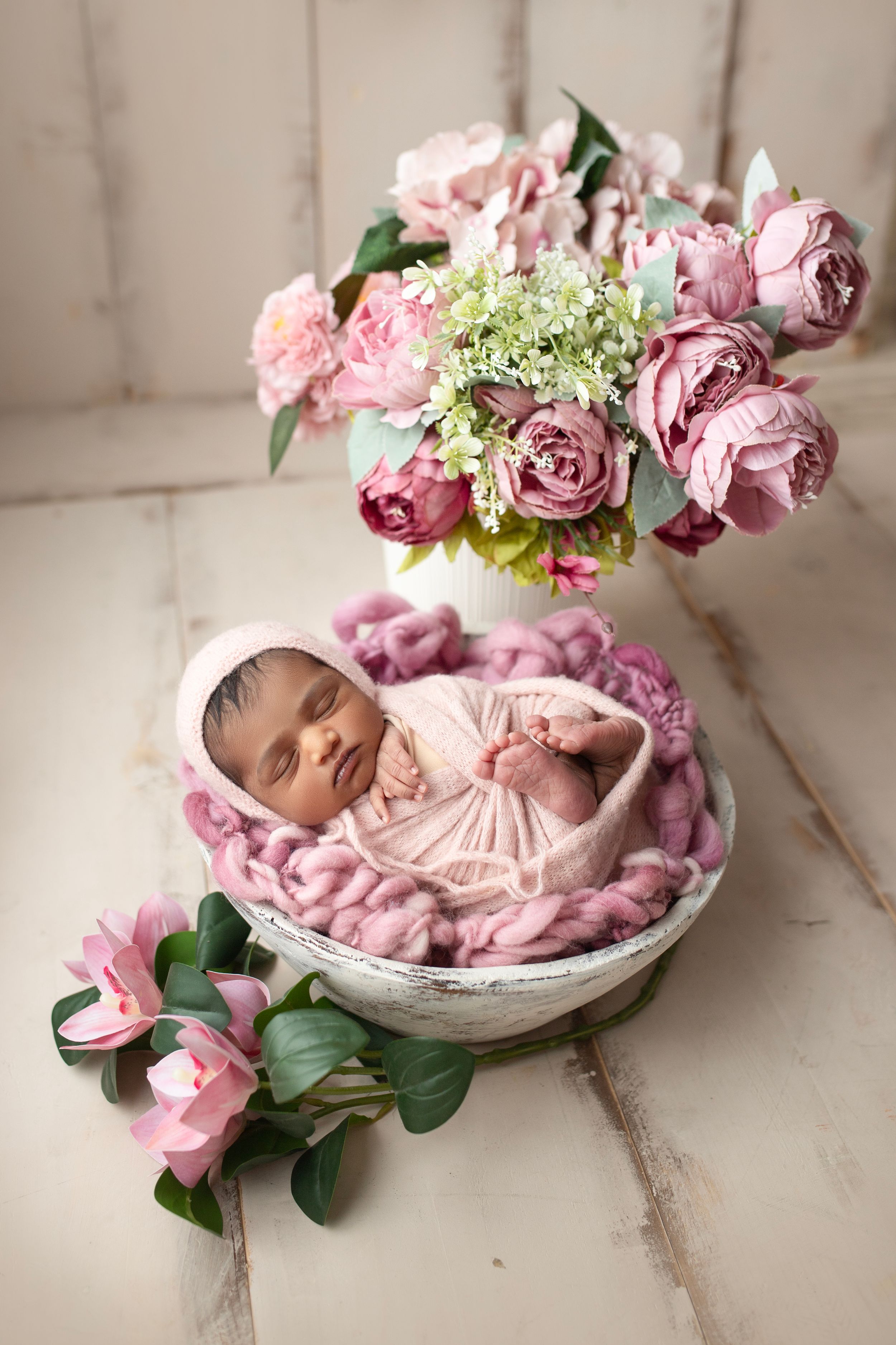 Newborn photography with pink roses and baby in pink knit blanket.