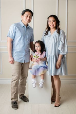 Family portrait with coordinating blue and purple outfits against neutral wall.