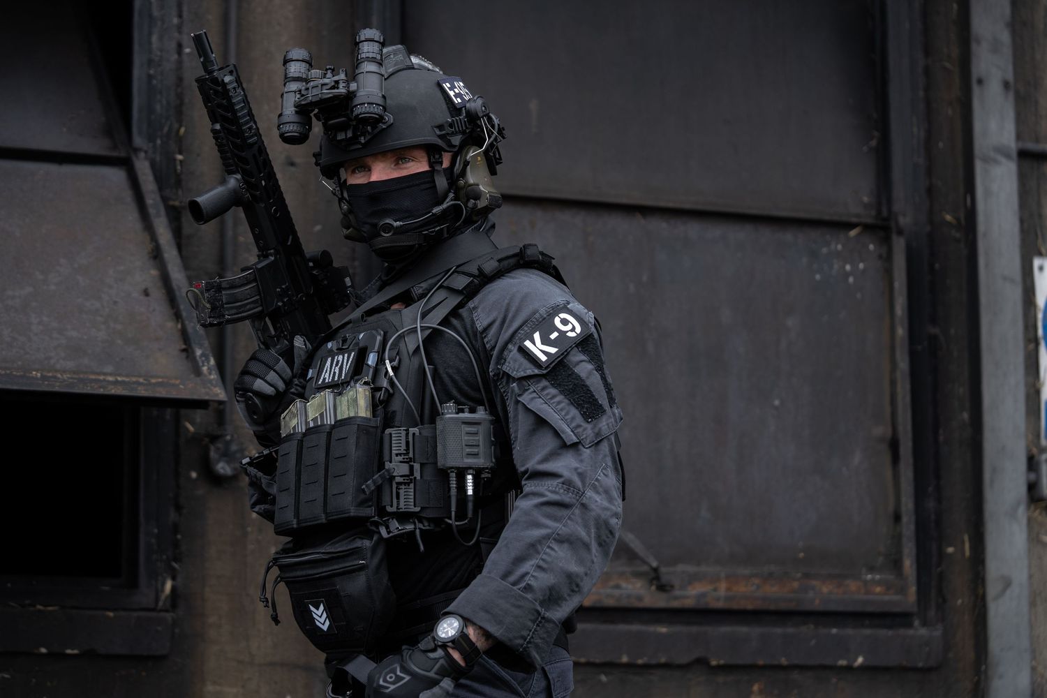 Close-up of gloved hands holding a pistol with mounted optics against dark background.