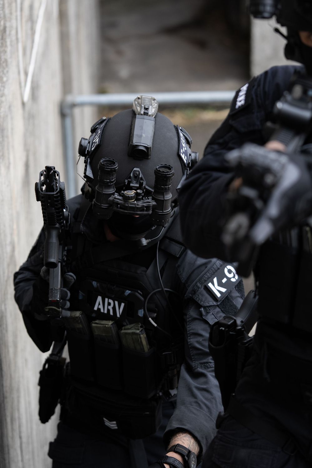 Special forces tactical team members in black gear performing a coordinated operation with weapons drawn.