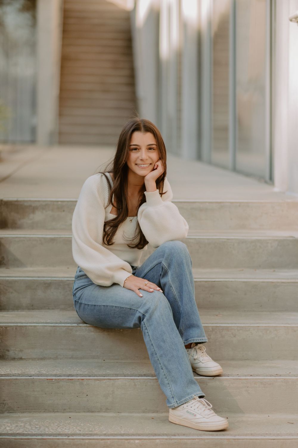 Giada, a Blythe Photo senior, poses for her senior portraits on concrete stairs, wearing a white sweater and jeans.