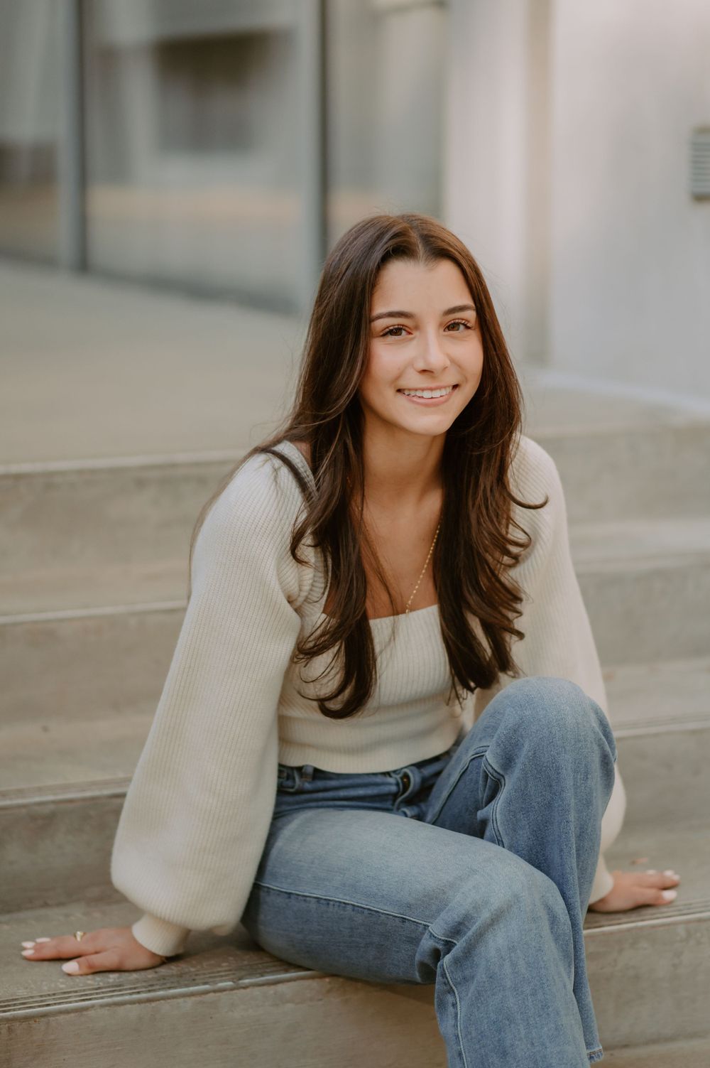 Giada smiles and sits on outdoor concrete steps, wearing a white sweater and jeans.