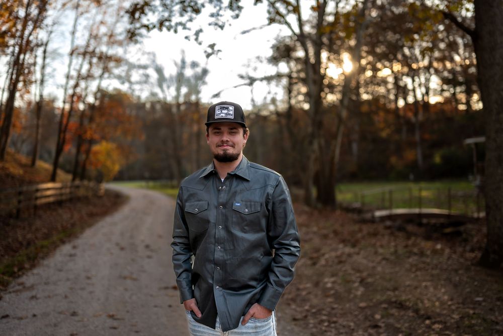 Person in denim jacket poses against autumn forest backdrop during golden hour sunset.