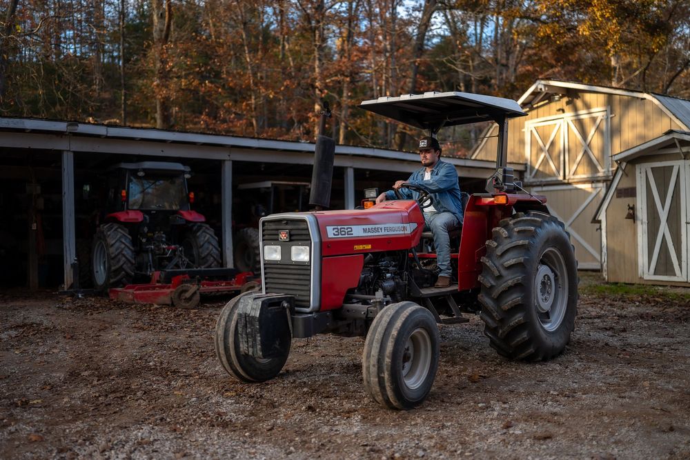 Row of vintage tractors parked in front of a barn during autumn season.