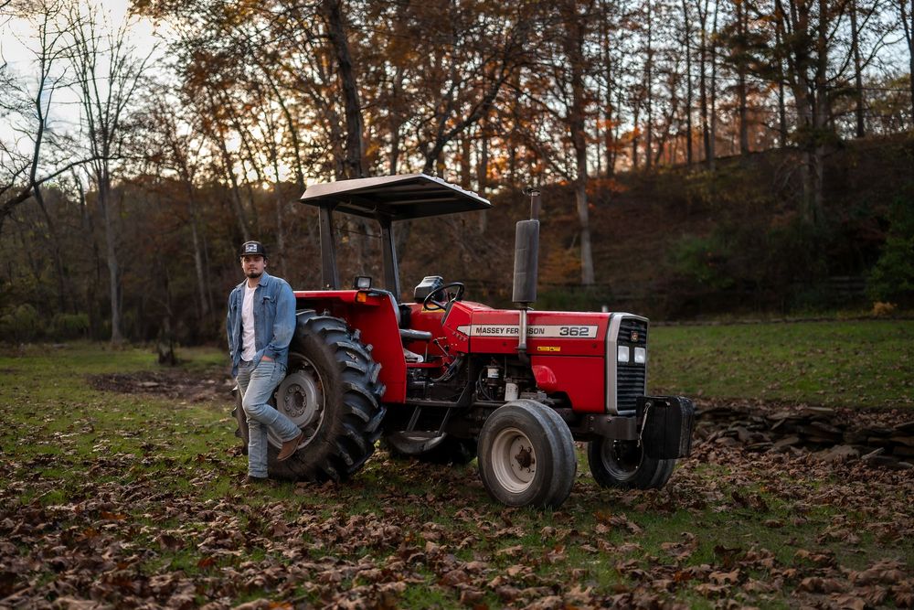 Red vintage tractor parked among fallen leaves in wooded area during golden hour.