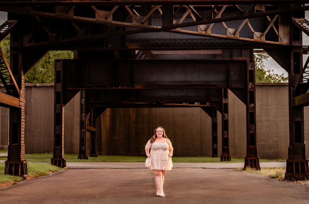 Person in light dress walking under industrial covered bridge structure.