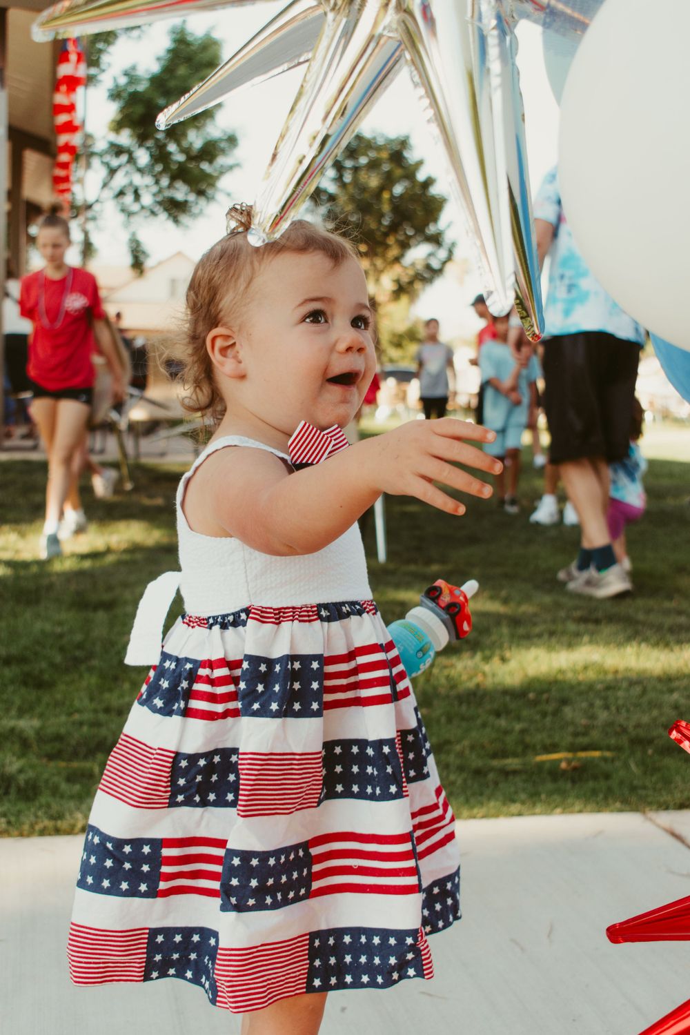 Baby wearing patriotic American flag dress at outdoor summer event.