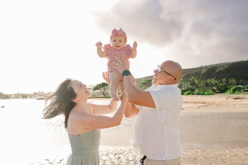 A parent and child play together on a sunny beach, lifting and spinning in a joyful moment.