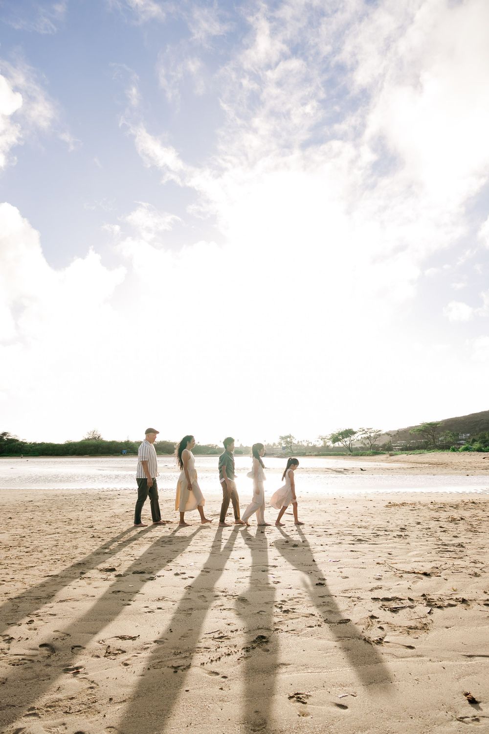Silhouettes of people walking on a sandy beach at sunset casting long shadows on the sand.
