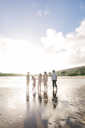 A group of people standing together on a sunlit beach with reflections in the wet sand during golden hour.