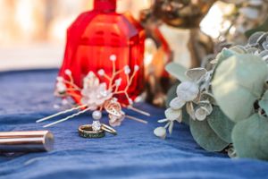 Wedding rings displayed on blue tablecloth with red lantern and floral decorations.