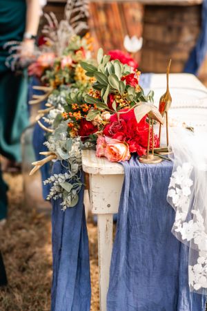 Elegant floral arrangement with red roses and eucalyptus on a white pedestal with flowing blue fabric.