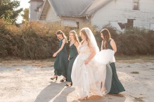 Bridesmaids in teal dresses walking with bride in white gown during sunset photo session.