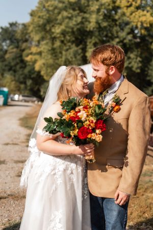 Wedding couple sharing intimate moment with fall-colored bouquet outdoors.