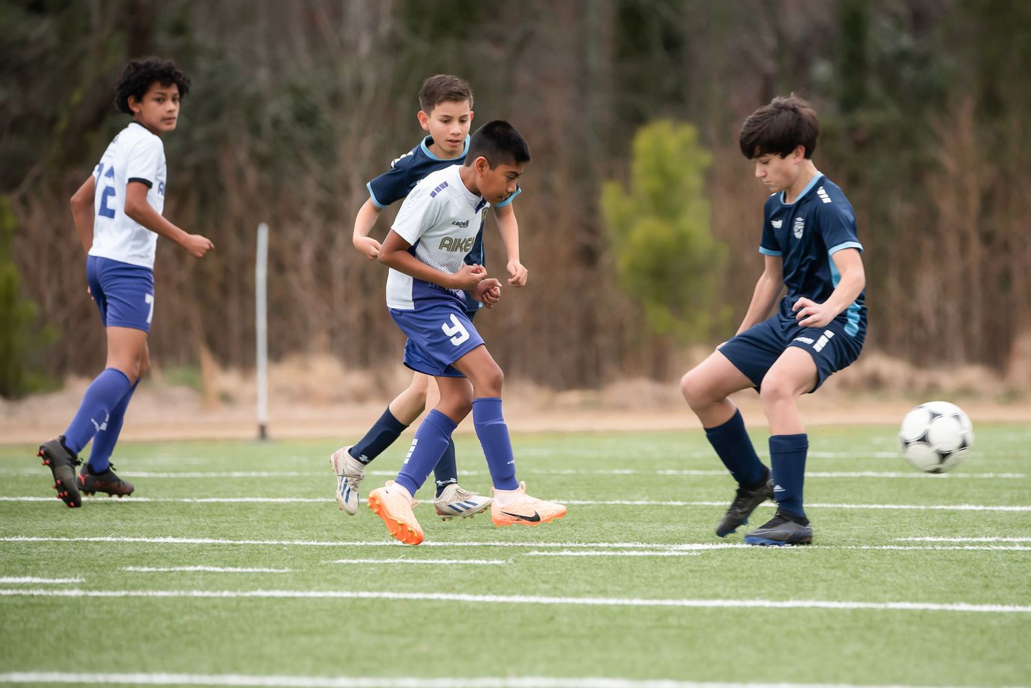 Soccer players in white and navy jerseys engaging in a competitive match on an outdoor field.