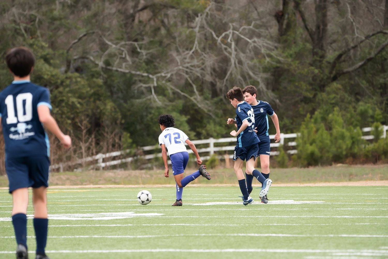 Youth soccer players compete on a green sports field with a white sideline.
