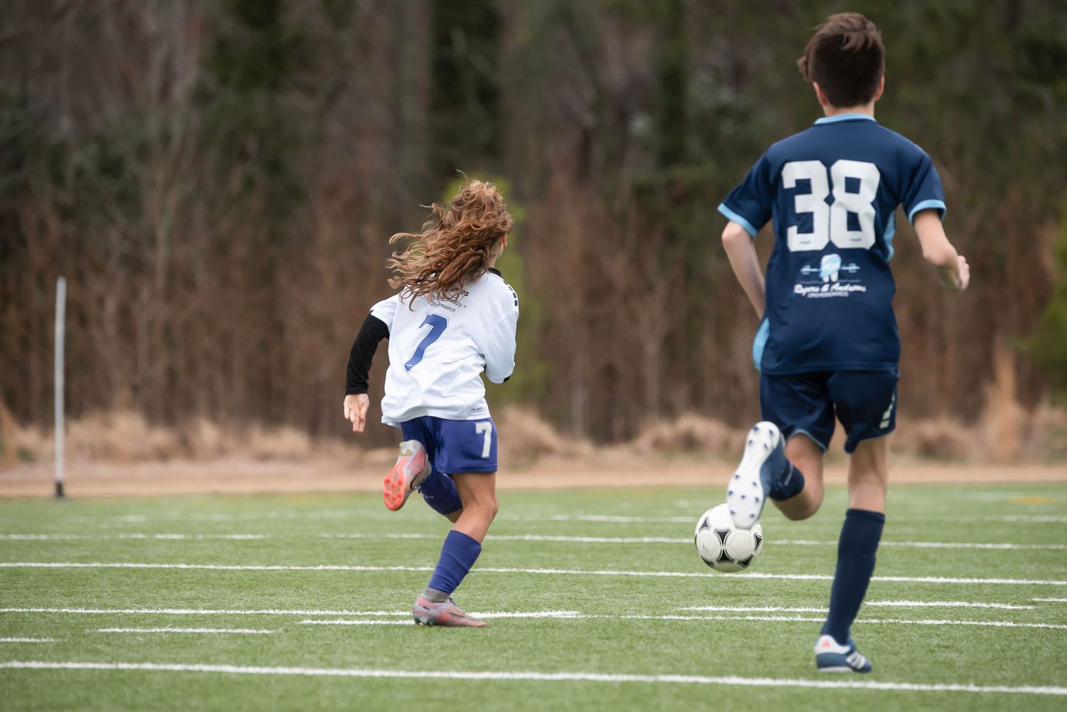 Players chase after a soccer ball on a sunny day during a match.