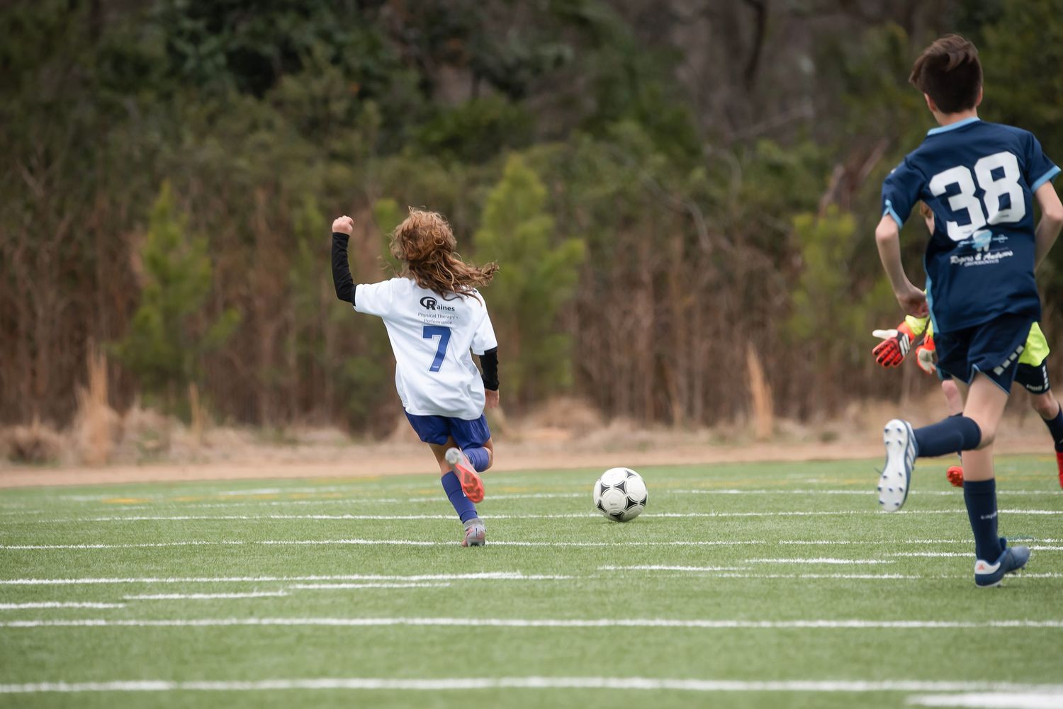 Soccer match action with players running on artificial turf field.