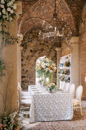 Elegant wedding reception setup in rustic stone arched venue with white tablecloths and floral decorations.