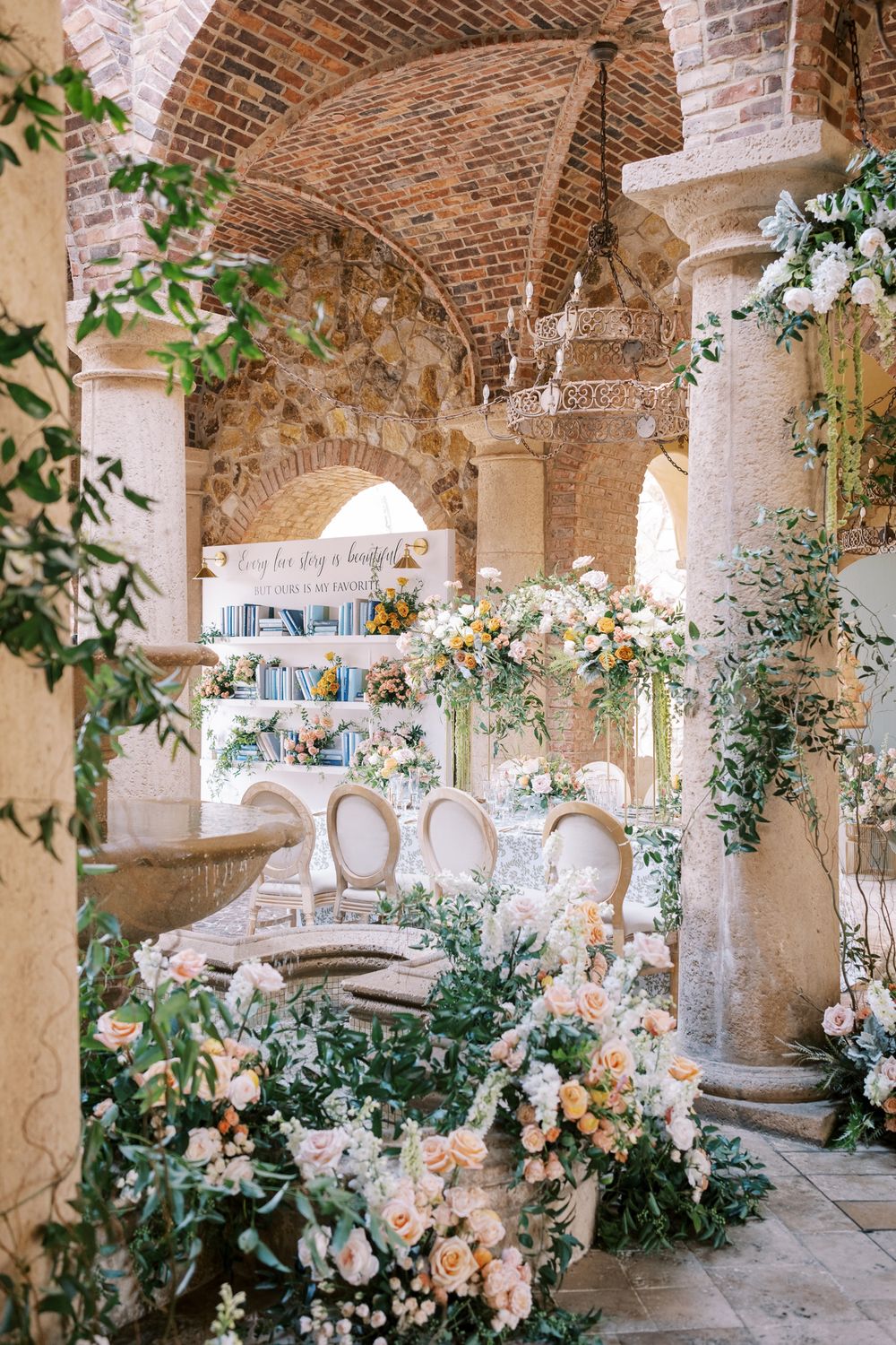 Elegant wedding venue with stone arches, bookshelves, and lush floral arrangements featuring white and peach blooms.