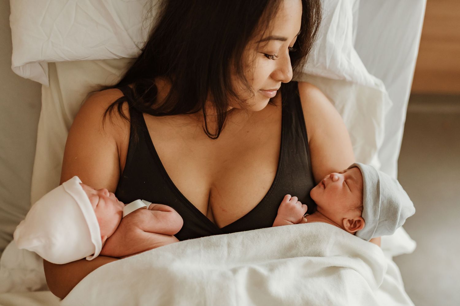 baby swaddled in their bassinet with parents hands on them in a hospital room