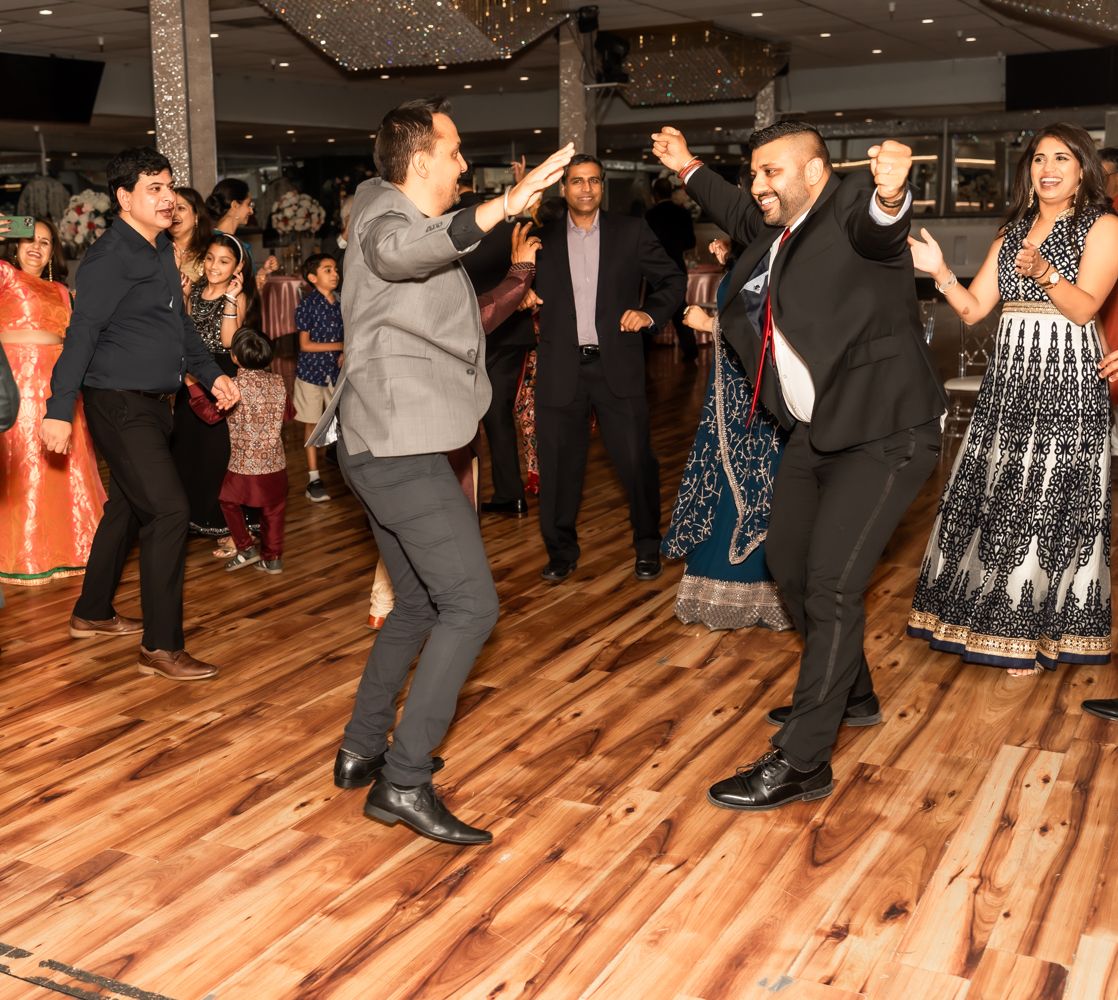 People dancing and celebrating on a hardwood dance floor at a formal event with festive lighting.