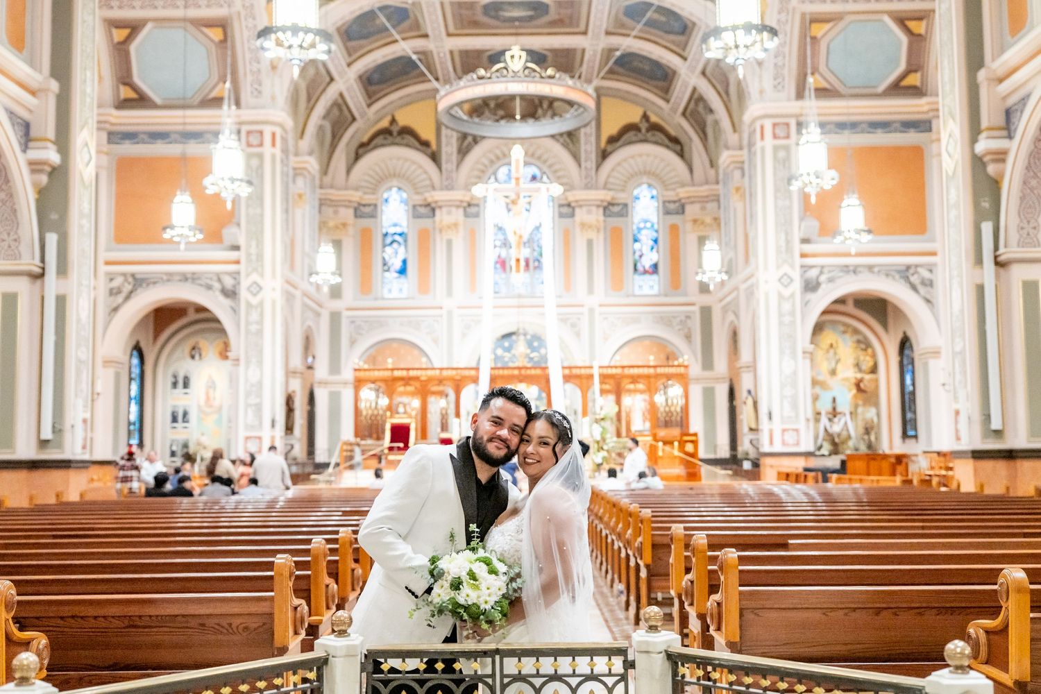 Bride and groom embrace at the altar of an ornate church with golden arches and stained glass windows.