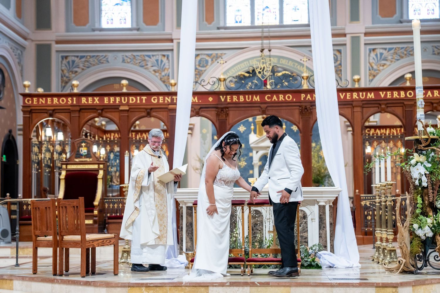 Bride and groom exchange vows at ornate church altar with officiant during elegant wedding ceremony.