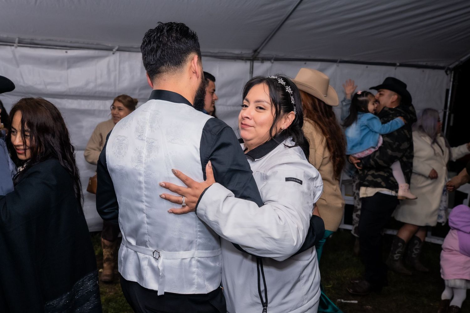 Couple dancing together at an indoor event under a white tent with guests celebrating in the background.