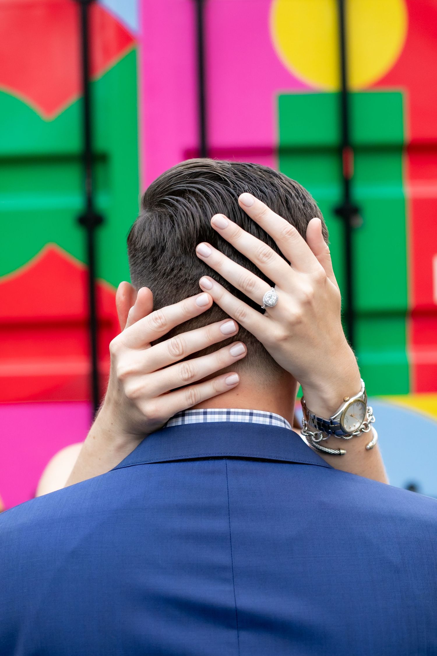 Two hands covering the back of a head against a colorful geometric wall background.