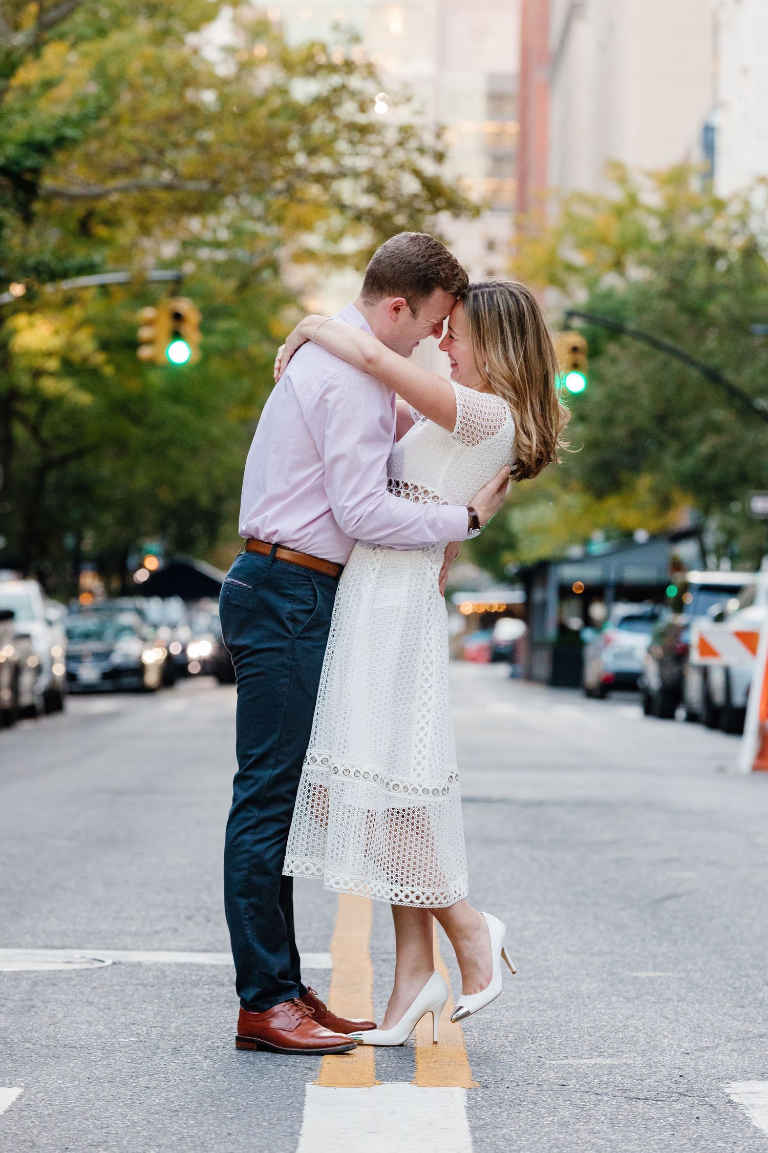 A romantic moment on a city street as a couple in white dress and pink shirt embrace in late afternoon light.