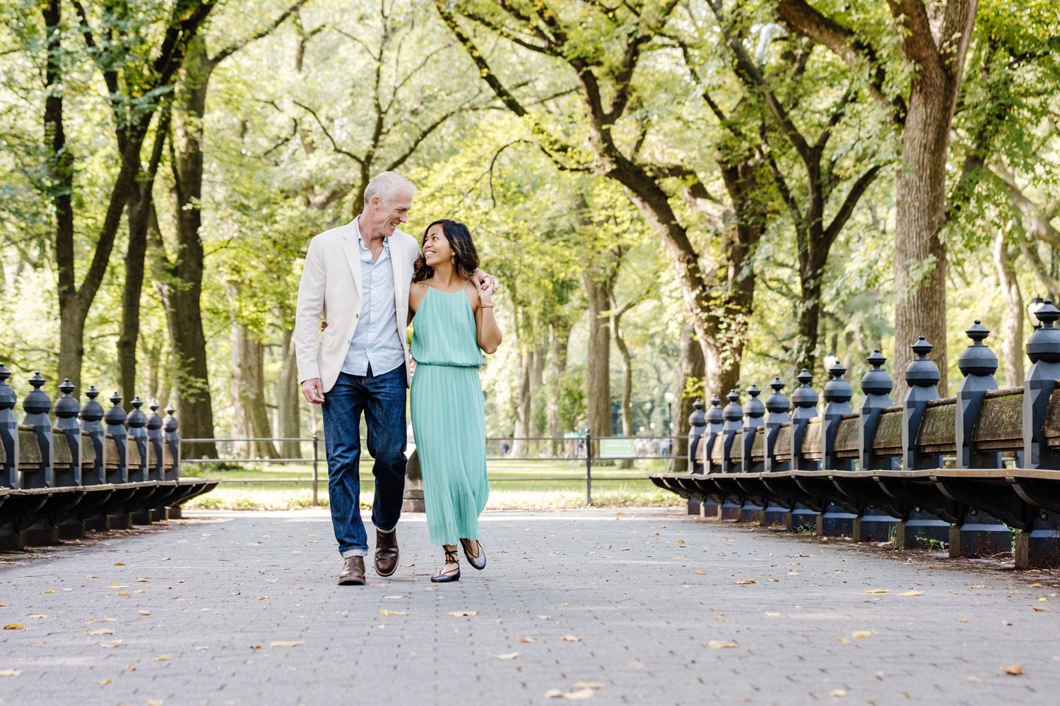 A couple walks together on a tree-lined pathway in a park during a sunny spring day.