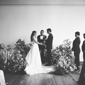 Black and white panoramic sequence showing a wedding ceremony with floral arrangements in an elegant indoor setting.