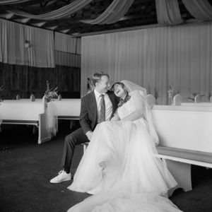 A black and white wedding photo showing a couple sitting together in an elegantly draped reception venue.