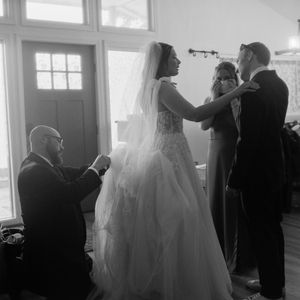 Black and white wedding preparation photos showing a bride in her dress getting ready with others in a sunlit room.