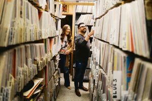 A couple browses through vinyl records in a cozy record store's narrow aisle surrounded by album shelves.