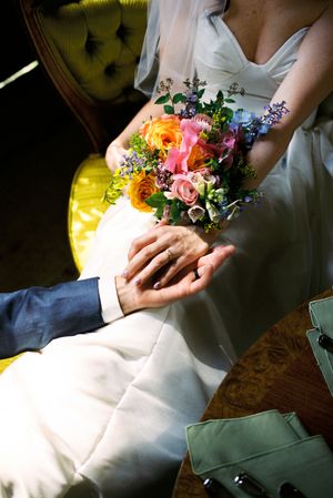 A colorful wedding bouquet of wildflowers and roses rests in white fabric-covered lap during a quiet moment.