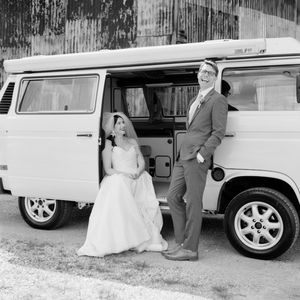 A black and white wedding photograph with a couple standing next to a vintage white Volkswagen van.