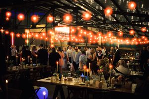 A dimly lit bar interior with glowing red lanterns overhead and patrons gathered at the counter on a busy evening.