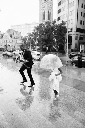 Black and white photos of a couple dancing playfully in the rain on a city street while wearing formal wedding attire.