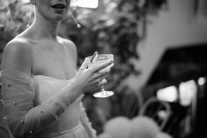 A black and white photograph shows someone in a formal dress holding a champagne glass at an evening event.