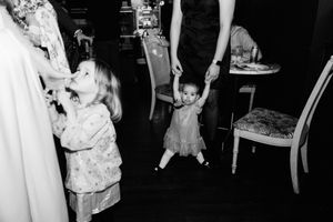 A candid black and white photograph shows two young children playing in a room with furniture.