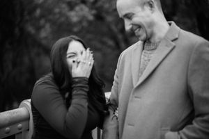 A black and white candid photo shows a laughing couple sharing a joyful moment together outdoors.