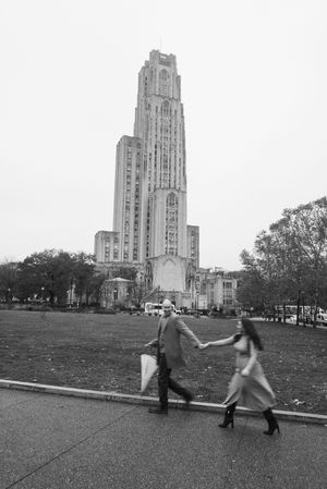 Two pedestrians pass by the Cathedral of Learning at the University of Pittsburgh on an autumn day in black and white.