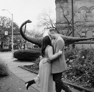 A romantic couple embraces while walking in an outdoor garden area in black and white photography.
