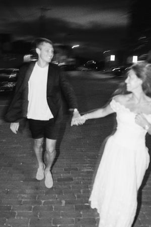 Black and white photo of a couple holding hands walking on cobblestone street at night.